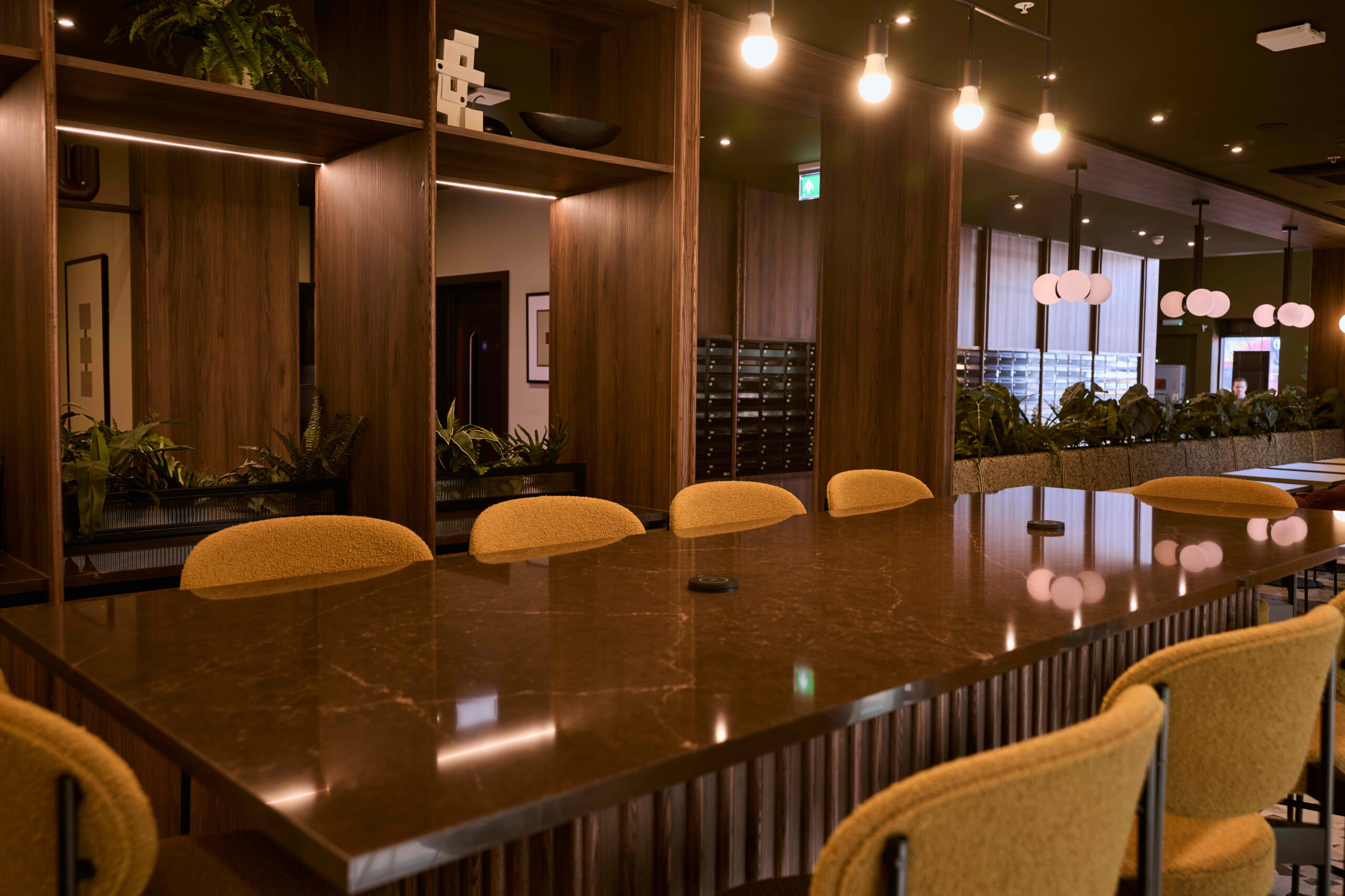 Modern ground floor lounge at The Rex co-living in Kingston, London, featuring a large communal table with yellow high-back chairs and wood panelling.