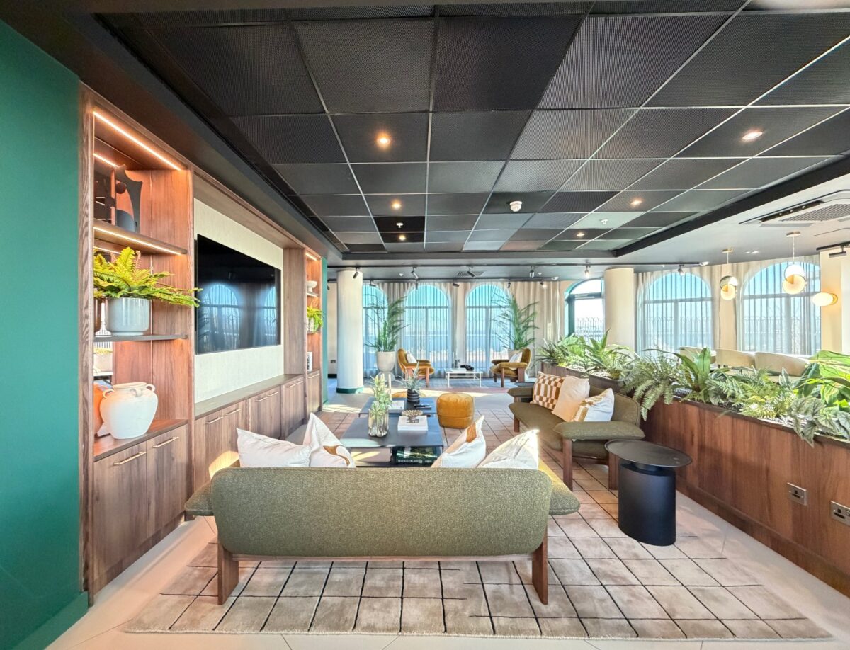 The expansive 7th-floor resident lounge at The Rex on Clarence Street, featuring mid-century modern green sofas, indoor plants, and floor-to-ceiling arched windows overlooking Kingston, London.